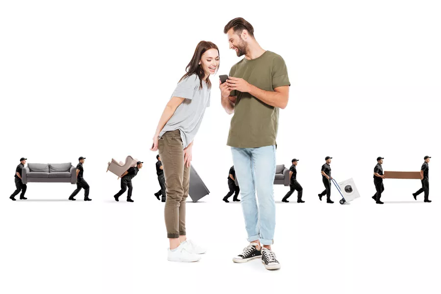 A happy couple looking at their phone, with multiple movers in the background moving furniture