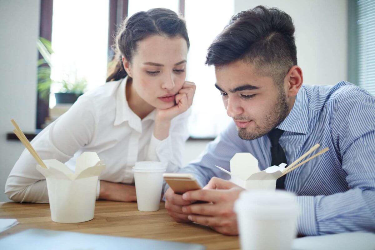 Couple using a cell phone while are eating chinese food