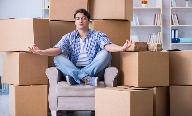 A man sits on a chair meditating while surrounded by boxes
