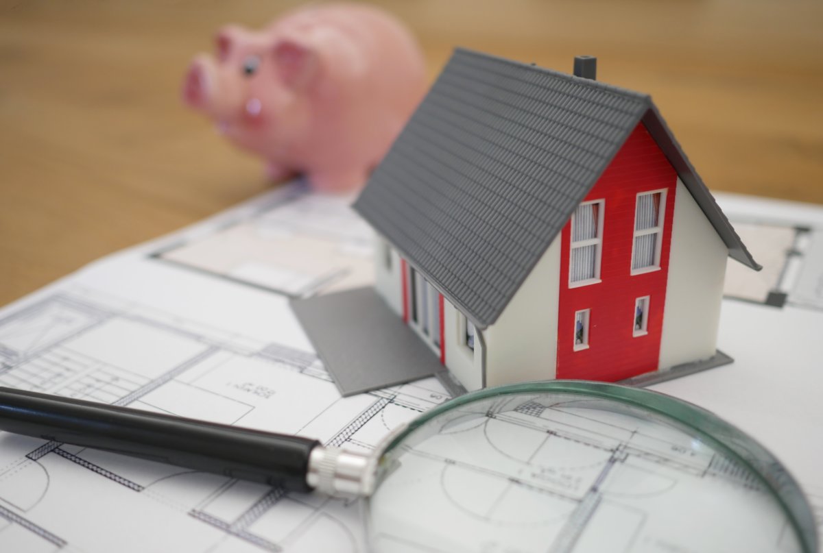 piggy bank in the background, toy house and magnifying glass in the foreground of image