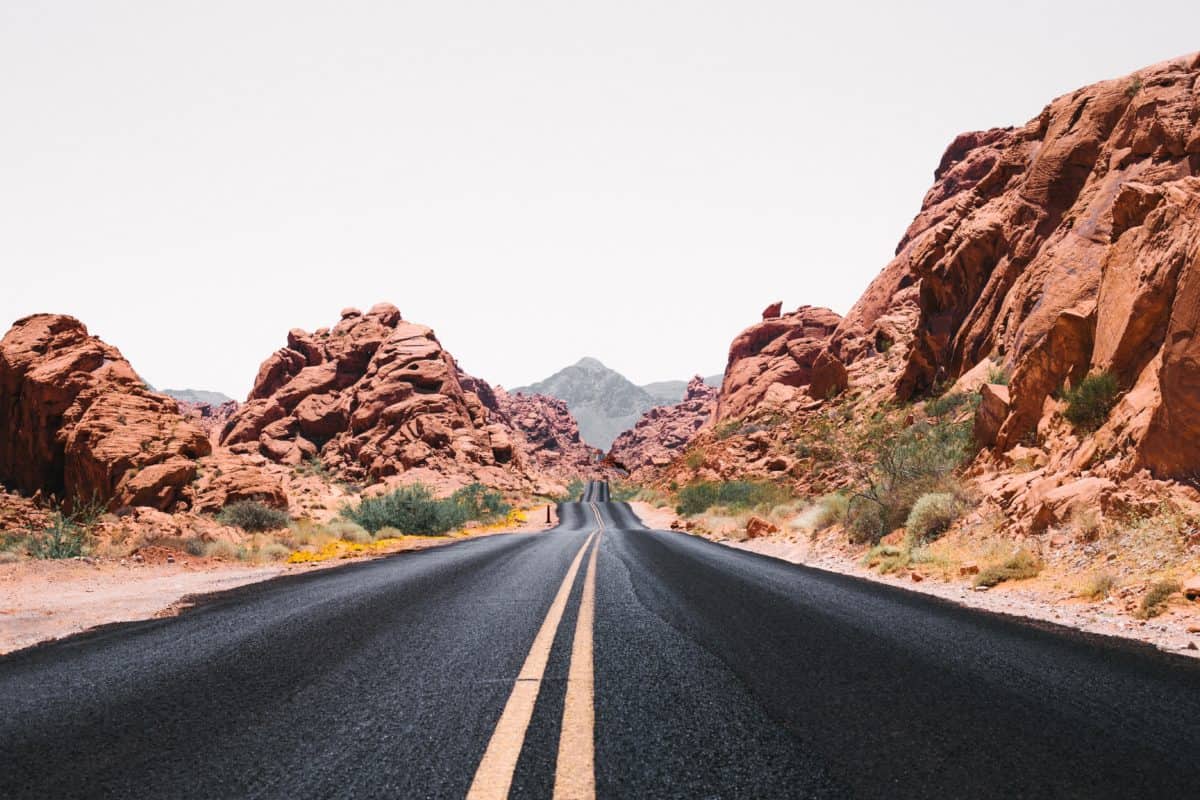 photo of empty highway during the day in desert with large boulders, rocks, and cliffs