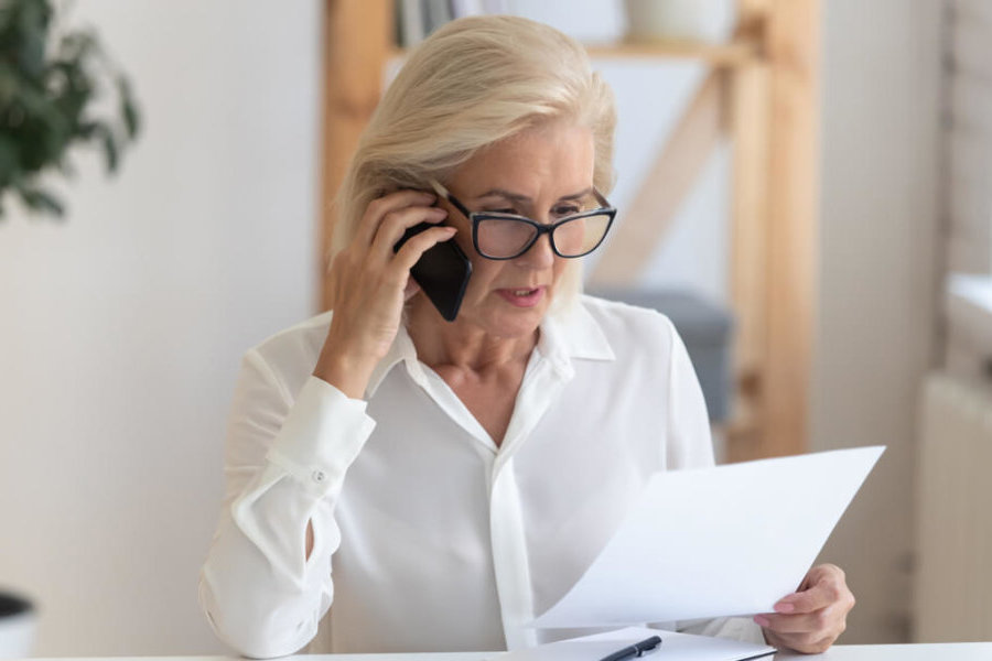 older woman making a phone call with paperwork in hand