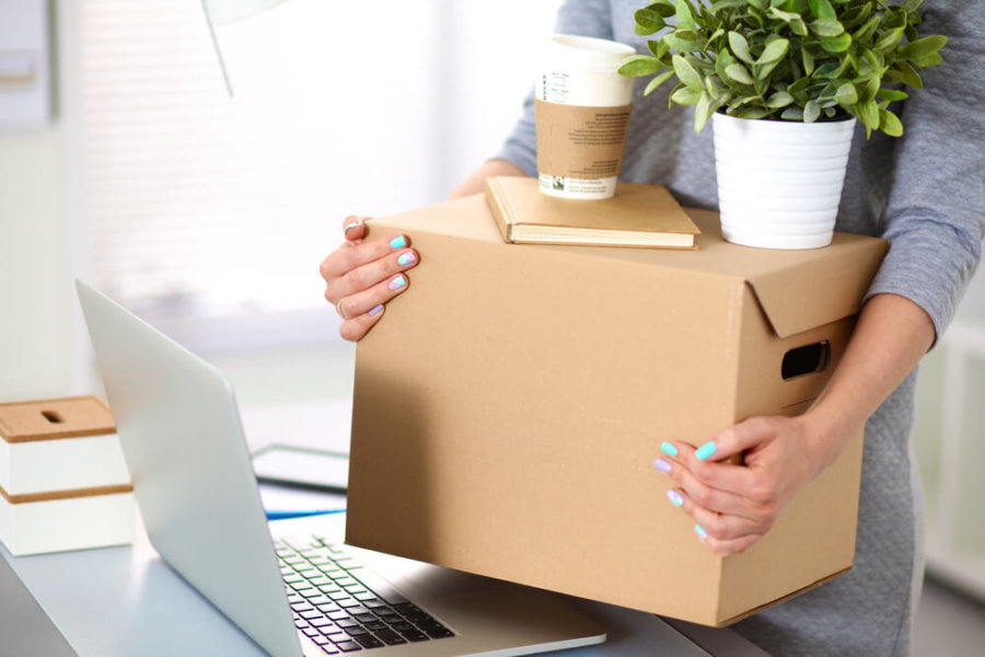 woman holding box above computer desk