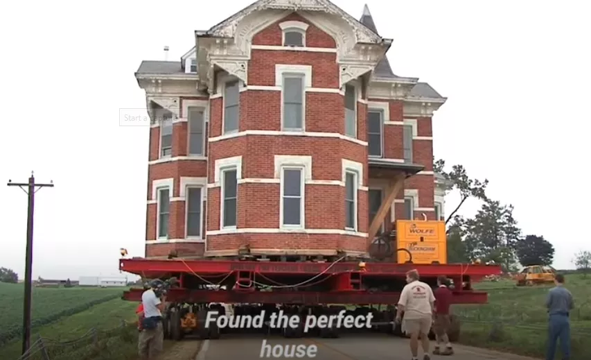 Four guys moving a house with a trailer.