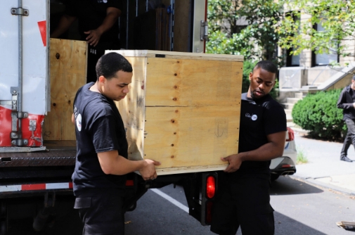 Two men downloading a wood box from the moving truck
